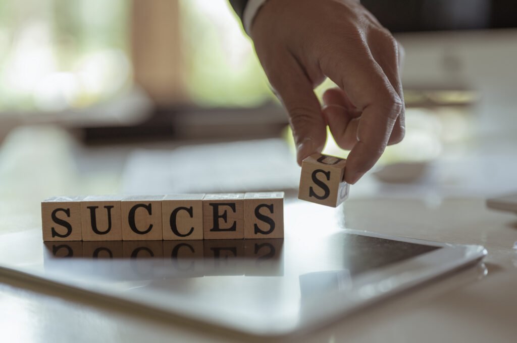 Hand placing the final letter tile to spell the word “SUCCESS” on a desk.