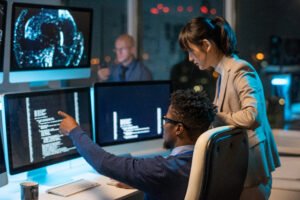 Two professionals working at computer monitors, one pointing at the screen.