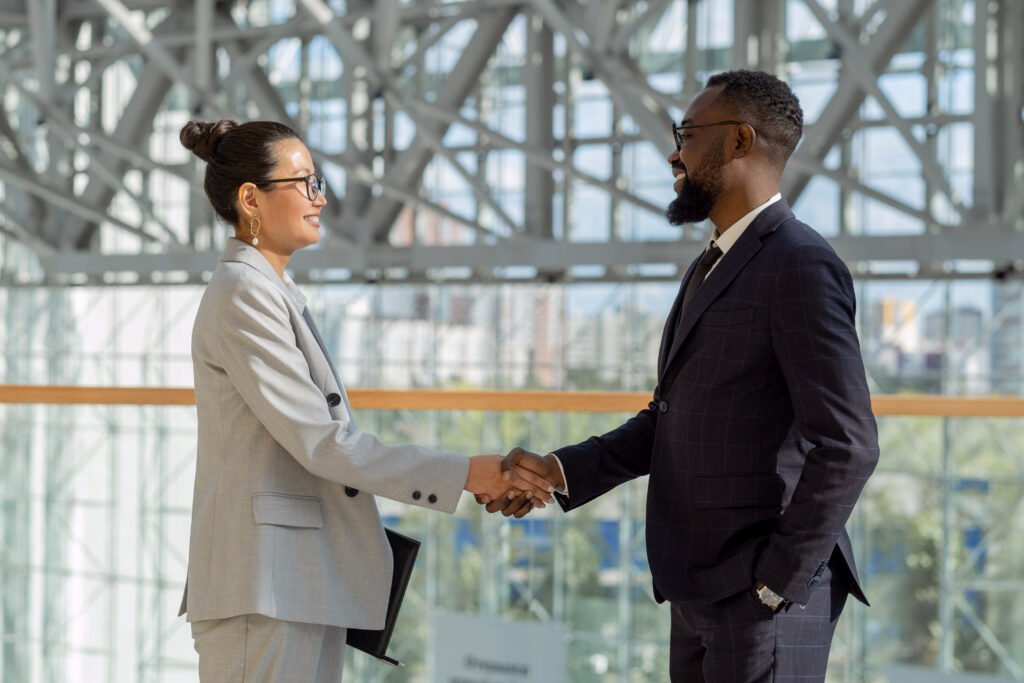 Two business professionals shaking hands and smiling in an office environment.