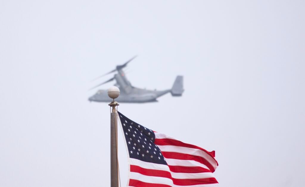 U.S. flag with a military Osprey aircraft flying overhead, representing federal service and national defense.