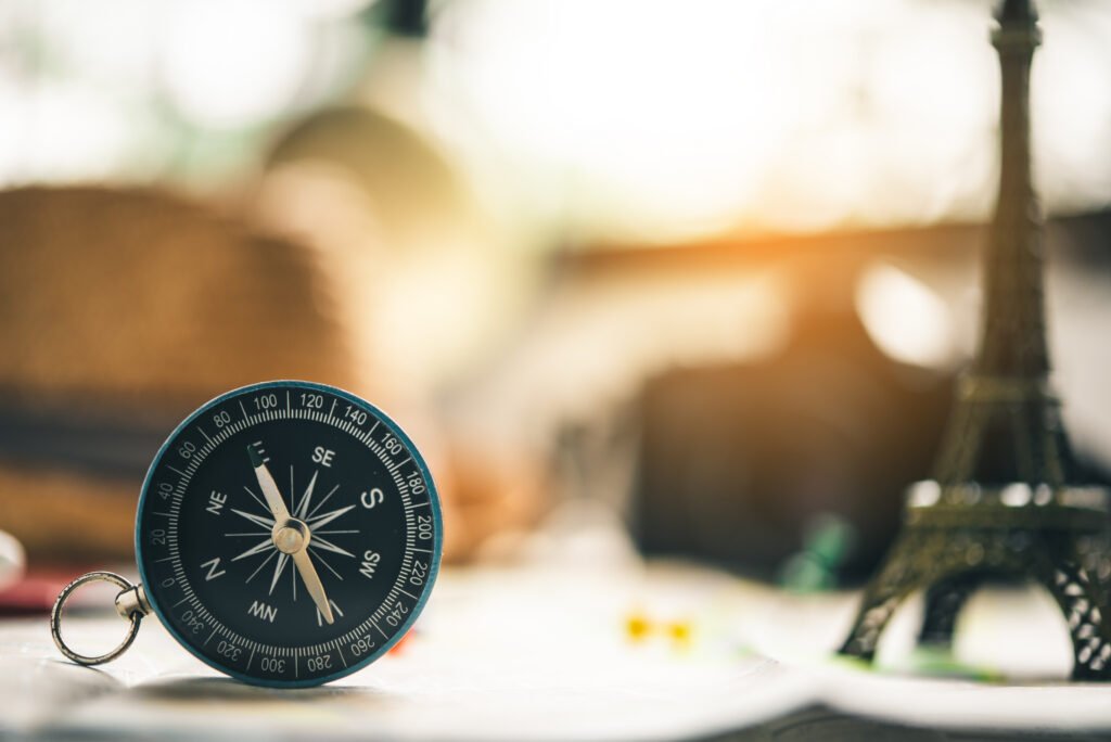 Compass placed on a desk with the Eiffel Tower blurred in the background.