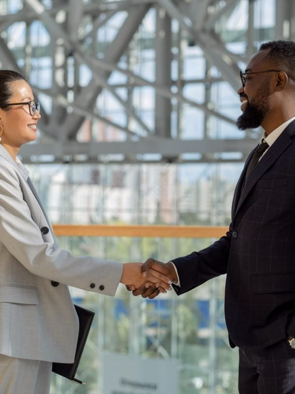 Two business professionals shaking hands and smiling in an office environment.